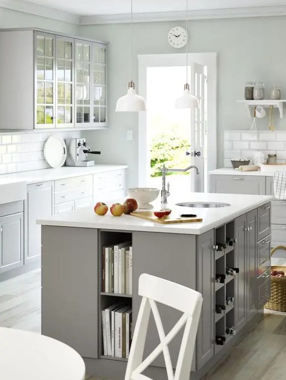 a Scandinavian kitchen with dove gray cabinets, white countertops and a white tile backsplash, a gray kitchen island with open storage for books and wine bottles and drawers