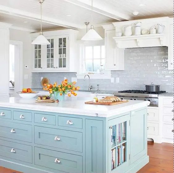 A white farmhouse kitchen with a glossy white tile backsplash, a cheerful blue kitchen island with book storage and drawers is a smart idea and a touch of color