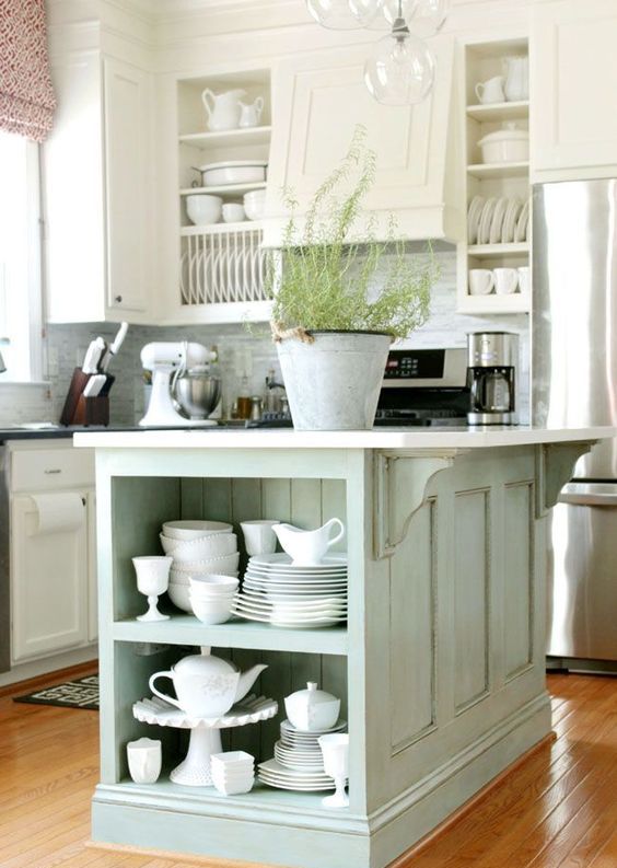a white farmhouse kitchen with shaker-style cabinets, a mint green kitchen island with open shelves for storage and stainless steel appliances