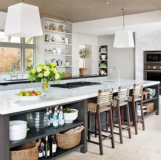 a white farmhouse kitchen with planked cabinets and walls, built-in appliances and an oversized gray kitchen island with dining area and lots of open shelves for storage
