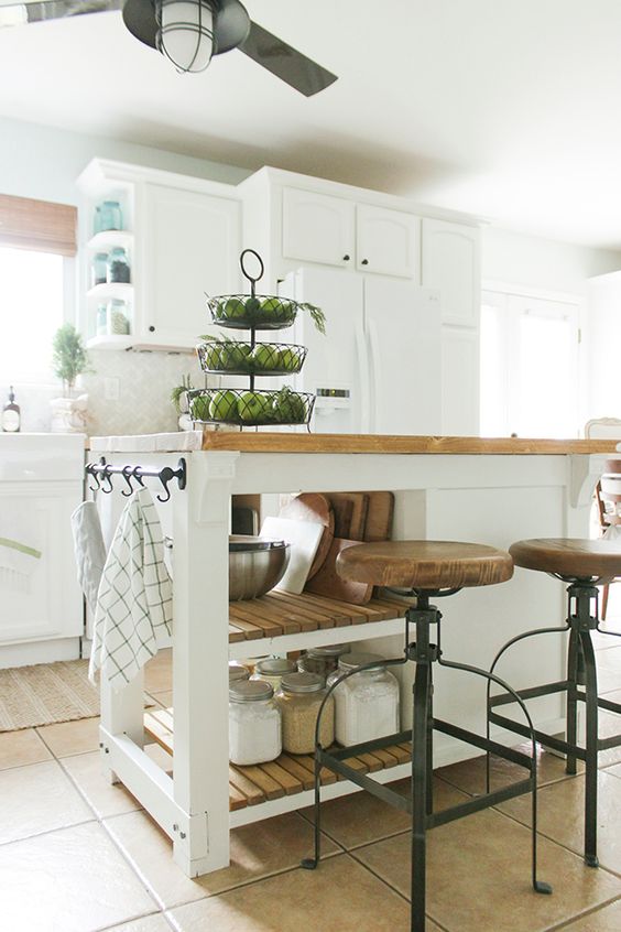 a white farmhouse kitchen with shaker cabinets, a small kitchen island with open shelves and an enclosed storage compartment