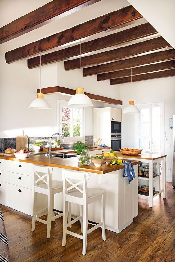a white farmhouse kitchen with boarded cabinets and butcher block countertops, a kitchen island with open shelving and stained wood beams on the ceiling