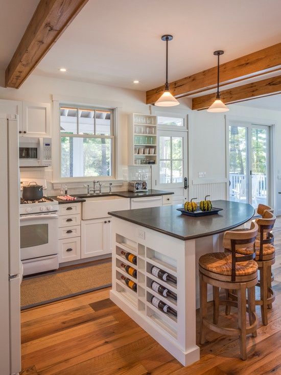 a white farmhouse kitchen with shaker-style cabinets, black countertops, and a rounded island with wine storage