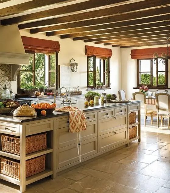 a charming farmhouse kitchen with wood beams on the ceiling, neutral cabinets, black countertops and a tan kitchen island with drawers and boxes for storage