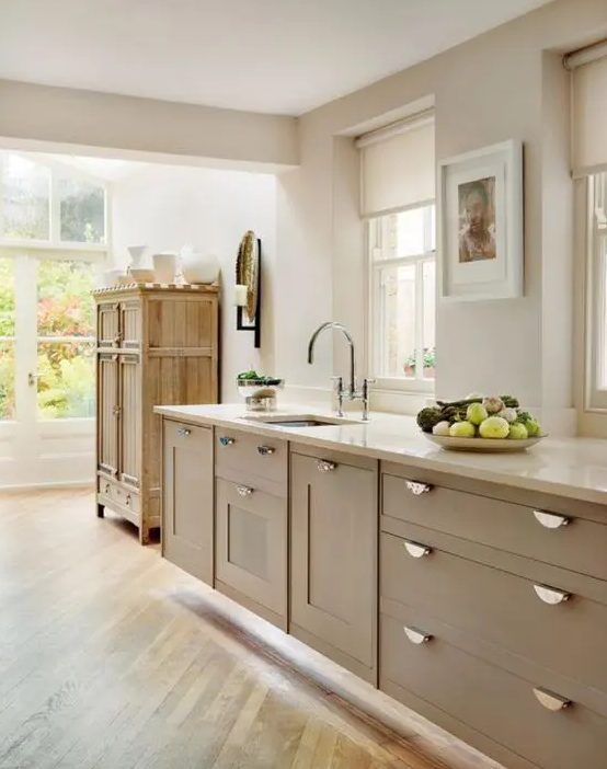 A beautiful taupe kitchen with shaker cabinets, vintage knobs, white stone countertops and a rustic vintage cabinet for storage