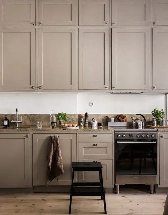 A stylish and atmospheric taupe kitchen with shaker-style cabinets, sleek appliances, and a gray stone backsplash and countertop is very elegant