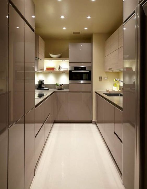 A super sleek and glossy taupe kitchen with no handles or built-in lights, with a pastel yellow sleek splashback and worktops