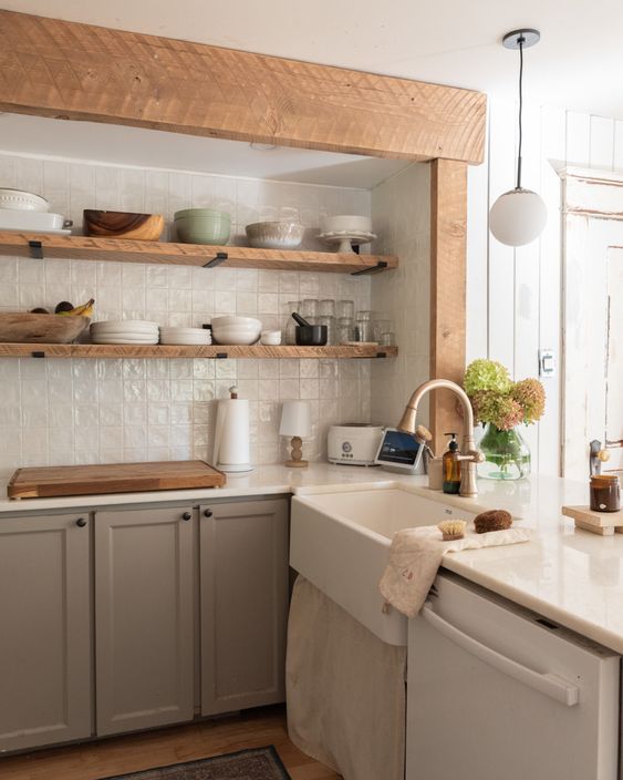 a taupe kitchen with open shelves instead of upper cabinets, white tiles on the back wall and a vintage sink and wooden beams