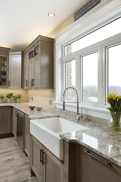 A traditional vintage kitchen with a white stone countertop, tan tile backsplash, built-in lights and a window with a view