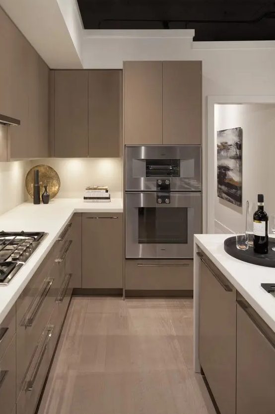 A sleek taupe kitchen with white stone countertops and a backsplash, built-in lights, and waterfall countertops is chic