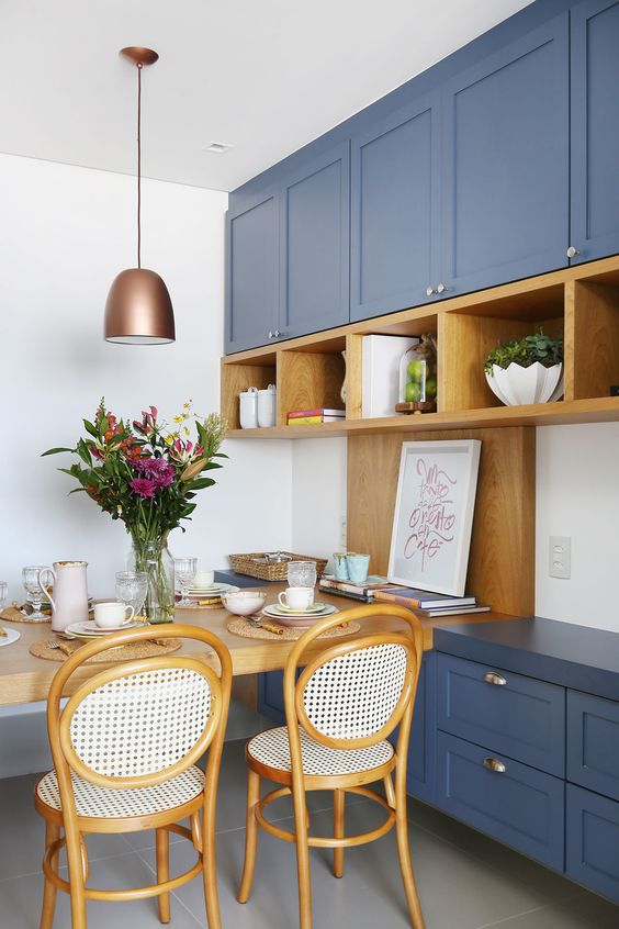 a bold blue kitchen with shaker cabinets, open stained shelving and a matching table and chairs, as well as a copper pendant lamp