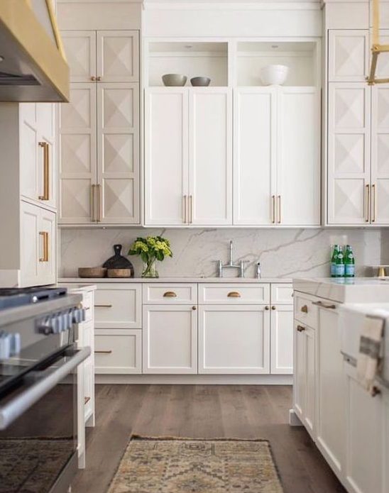a creamy Shaker-style kitchen with geometric cabinetry, a white marble backsplash and countertops, and gold and brass accents