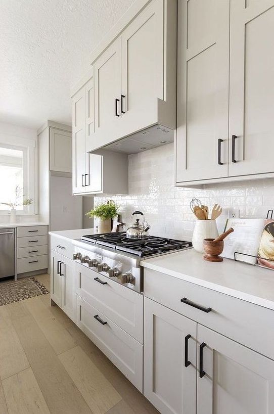 A dreamy and airy neutral kitchen with shaker-style cabinets, white tiles and countertops, and black handles is a beautiful space to cook in