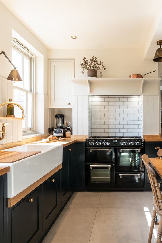 A fantastic bold black and white farmhouse kitchen with shaker cabinets, butcher block countertops, a white subway tile backsplash and brass hardware