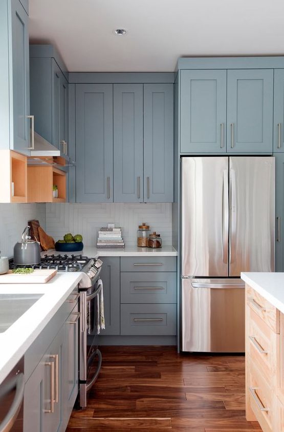 A light blue shaker-style kitchen with a white square tile backsplash, white countertops and stainless steel handles is super chic and airy