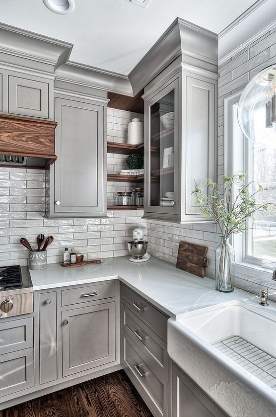 a light gray kitchen with shaker cabinets, white countertops, a white thin tile backsplash and touches of stained wood