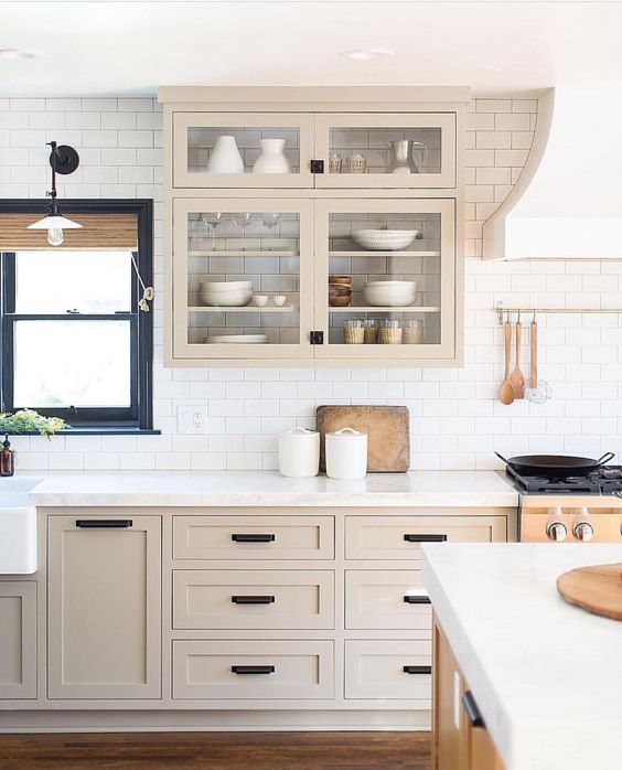 a light-stained farmhouse kitchen with shaker cabinets, black handles, white subway tile on the back wall, and a navy-framed window