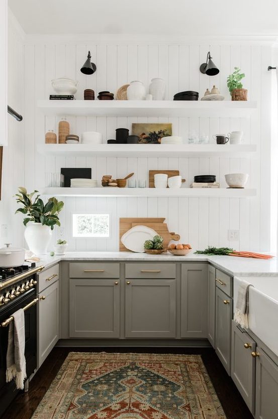 A pretty U-shaped kitchen with gray shaker-style cabinets, white countertops, white floating shelves, and brass and gold accents for elegance