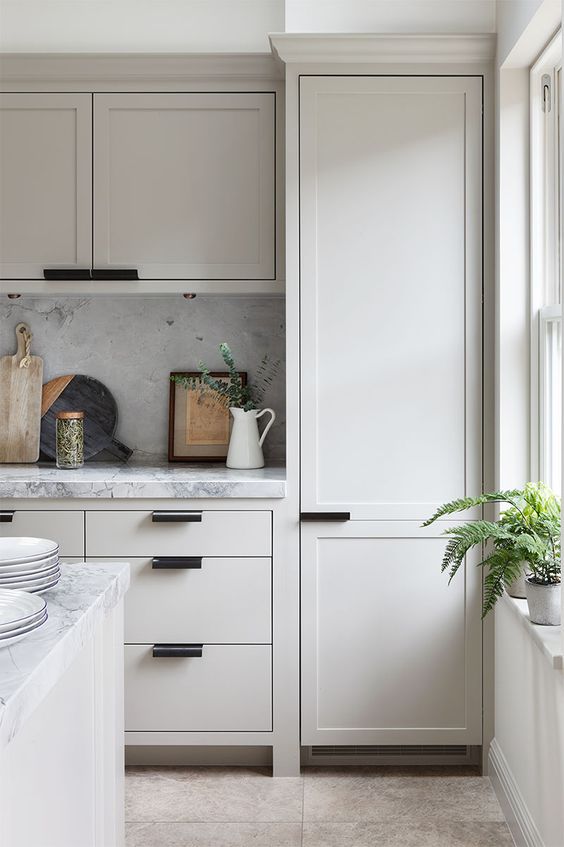 a super modern cream kitchen with shaker and traditional cabinetry, modern black handles and a white marble splashback and worktop