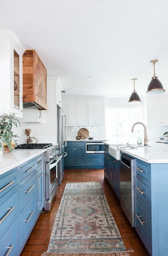 an airy kitchen with white and blue cabinets, white quartz countertops, a white backsplash and stainless steel handles, and a stained wood hood