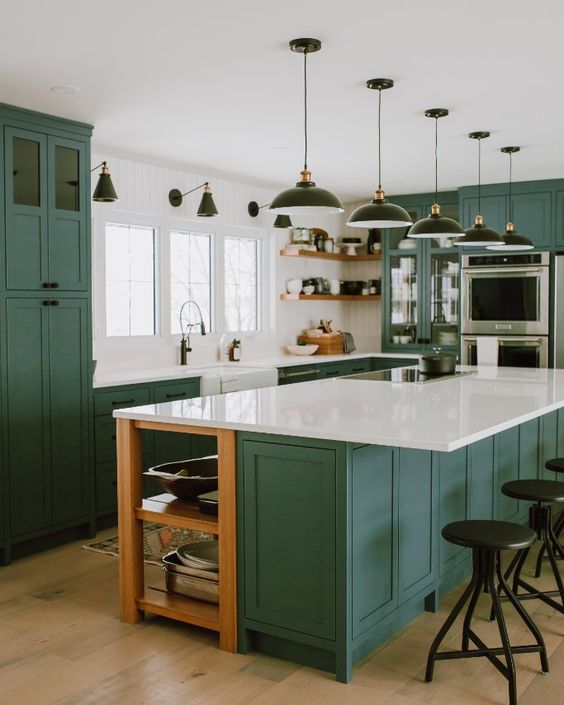 an emerald green kitchen with shaker-style cabinets, white stone countertops, black pendant lamps and sconces, and black stools
