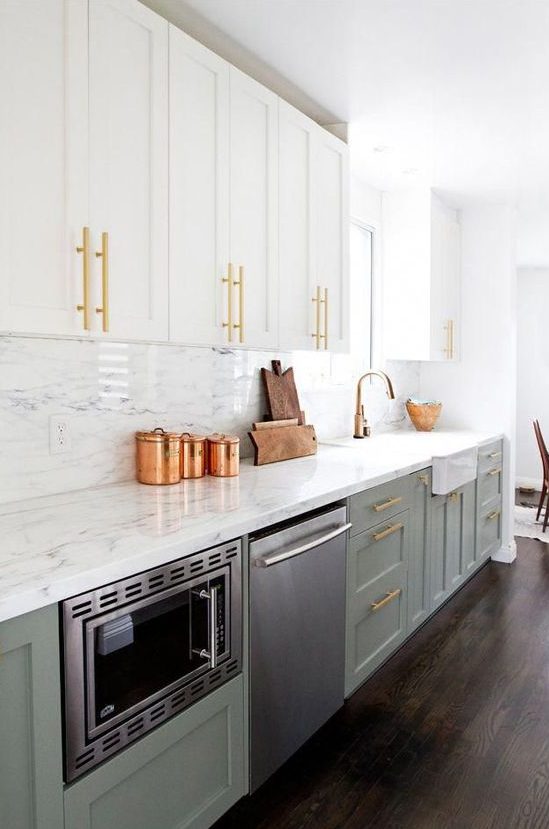 an exquisite two-tone kitchen with white and sage green cabinets, a white quartz backsplash and countertops, and touches of gold