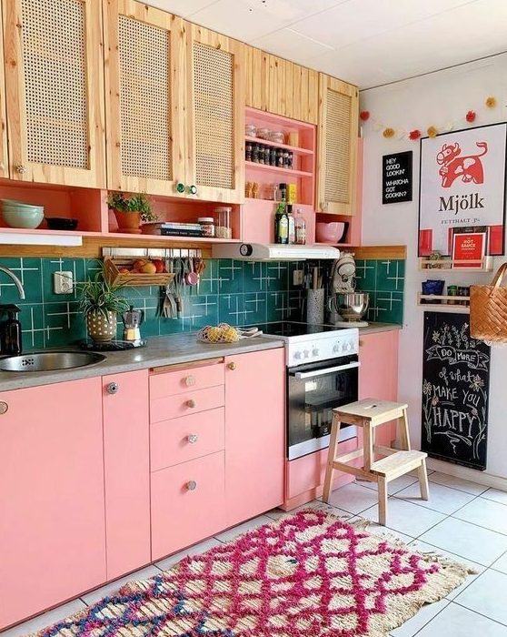 a bright maximalist kitchen with rattan and pink cabinets, a green tile backsplash, a bright printed rug, and colorful art