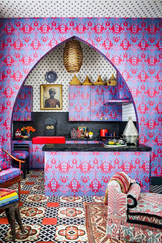a crazy maximalist kitchen with purple and pink wallpaper everywhere, a gold pendant lamp, black tiles and stone countertops, and a statement piece of art
