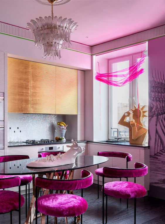 a stunning maximalist kitchen with white and gold ribbed cabinets, a white tiled backsplash, pink chairs and crazy sculptures