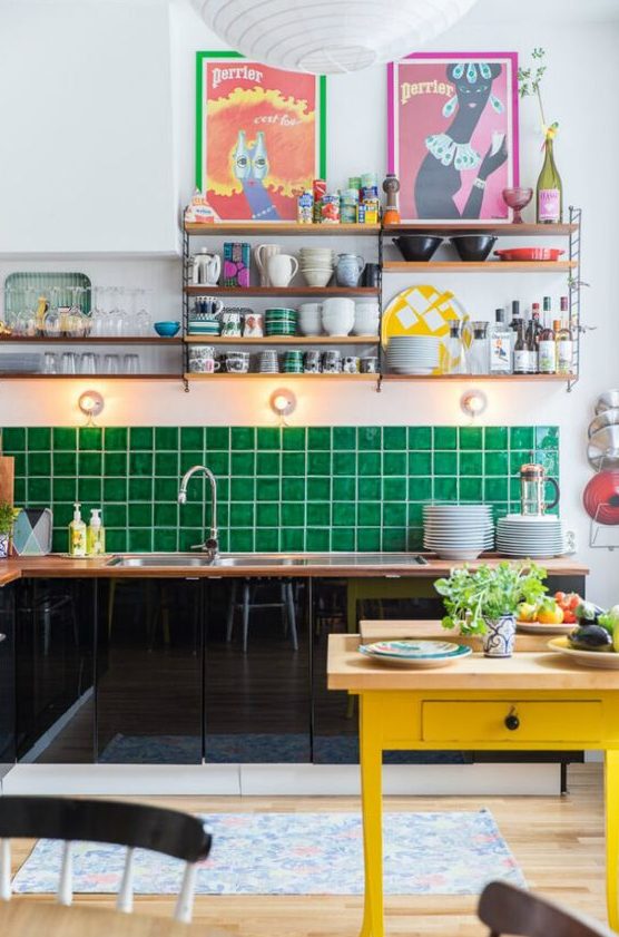 a maximalist kitchen with black sleek cabinets, an emerald green tile backsplash, a yellow table, colorful artwork and open shelving