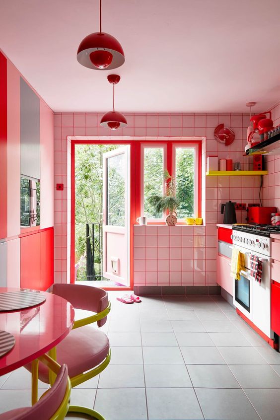 a maximalist kitchen with white tiles and red railings, blush and red cabinets, neon yellow shelves and neon yellow and pink chairs