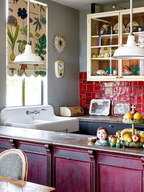 a vibrant maximalist kitchen with black and white cabinets, a red tile backsplash, a fuchsia island, a printed shade and vintage pendant lamps