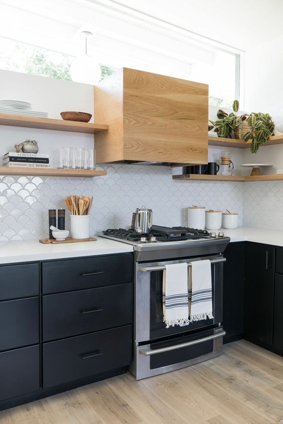 A chic mid-century modern kitchen with black cabinets, white countertops, white Moroccan tiles and light stained shelves