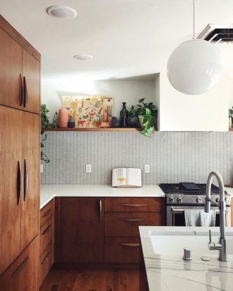 A chic mid-century modern kitchen with dark stained and white cabinets, white stone countertops and a white tile backsplash, as well as lights and lamps