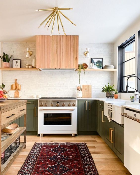 a cozy mid-century modern kitchen with green cabinets, light stained shelves, a range hood, white countertops and a wooden kitchen island