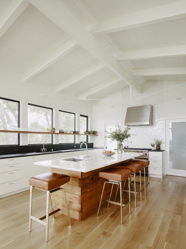A chic mid-century modern kitchen with white cabinets, black countertops and backsplash, wooden island and leather stools