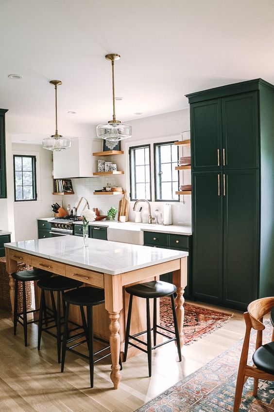 A dark green mid-century modern kitchen with shaker-style cabinets, white stone countertops, a tabletop kitchen island, and black stools