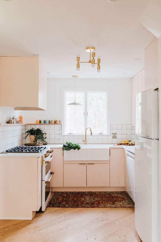 A pretty pink mid-century modern kitchen with a white square tile backsplash, white countertops and glamorous gold fixtures