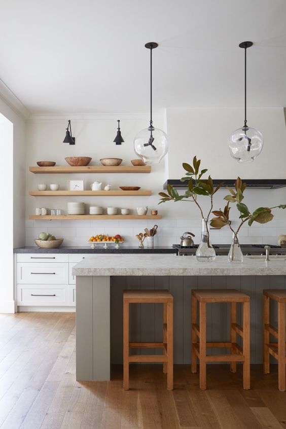 A cool mid-century modern kitchen with white shaker-style cabinets, a large range hood, a gray kitchen island, open shelving and cool lamps