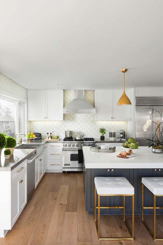 A mid-century modern kitchen with white cabinets, a white Moroccan tile backsplash, a navy kitchen island, white stools, pendant lamps and potted plants