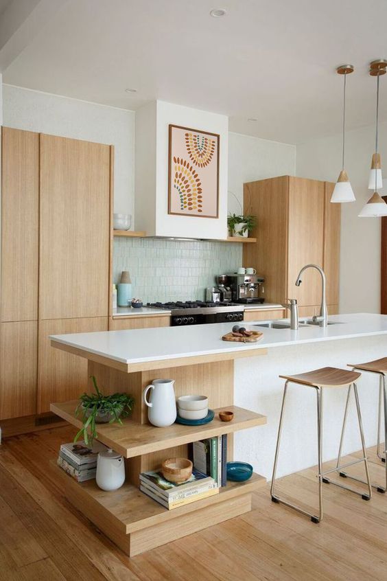 an airy mid-century modern kitchen with light stained cabinets, a white kitchen island with open shelves, a green tile backsplash, and pendant lamps