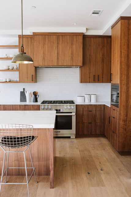 A mid-century modern kitchen with dark stained cabinets, a richly stained island, white stone countertops and a white thin tile backsplash