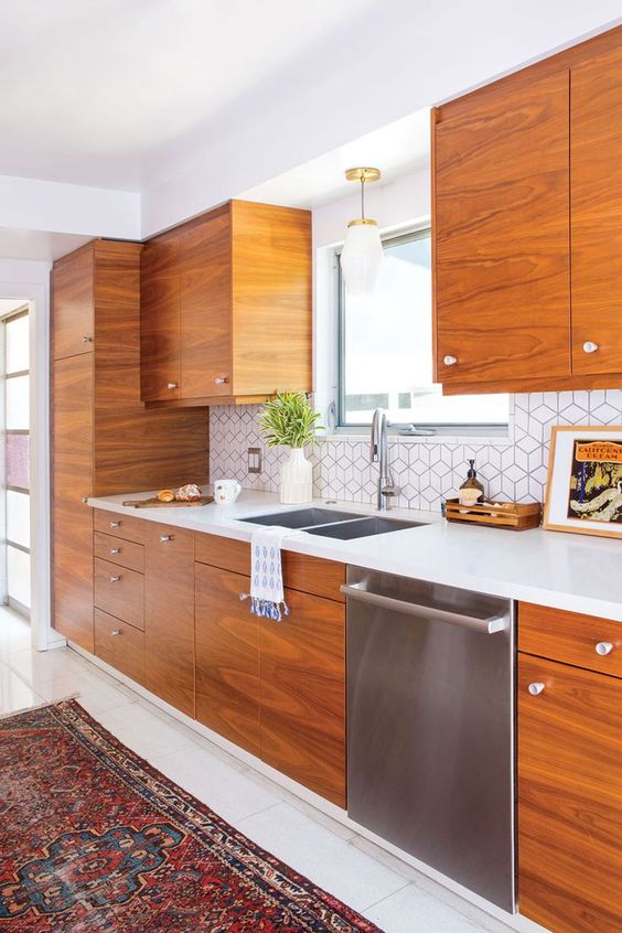 A mid-century modern kitchen with richly stained cabinets, a geometric tile backsplash, white stone countertops, and a printed rug