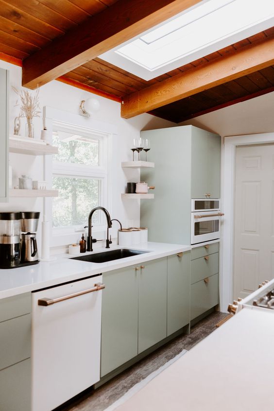 An inviting mid-century modern kitchen in pale green, a skylight, stained wood ceiling and white stone countertops
