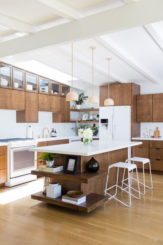 A dark stained mid-century modern kitchen with white countertops, white stools, pendant lamps, and gold fixtures is a beautiful space