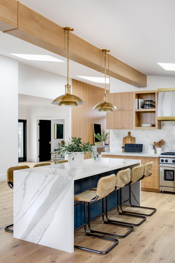 A beautiful mid-century modern kitchen with light stained cabinets, a white chevron backsplash and a navy blue kitchen island with a white marble countertop