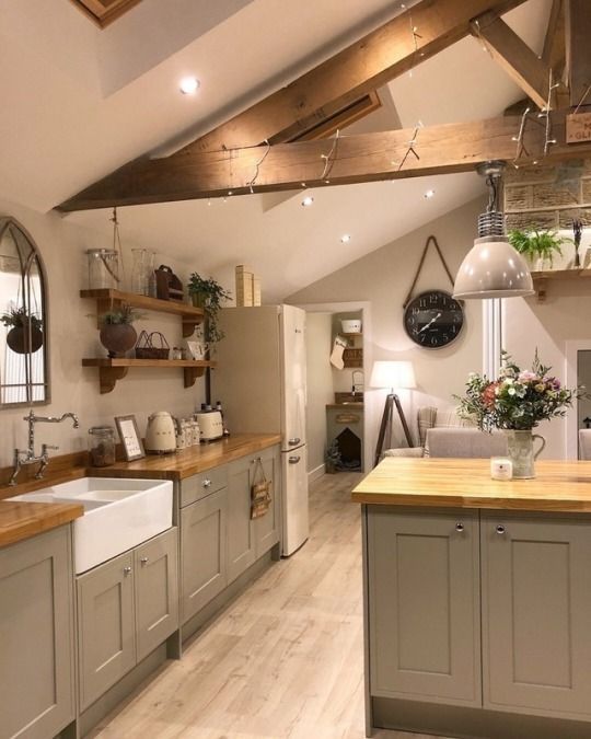 A gray farmhouse kitchen in the attic with butcher block countertops, open shelving and wooden beams, a mirror and a vintage faucet