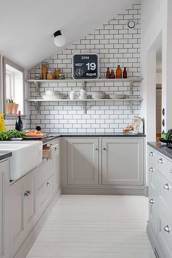 A gray Scandi attic kitchen with white subway tiles, black stone countertops, open shelving and neutral knobs is chic
