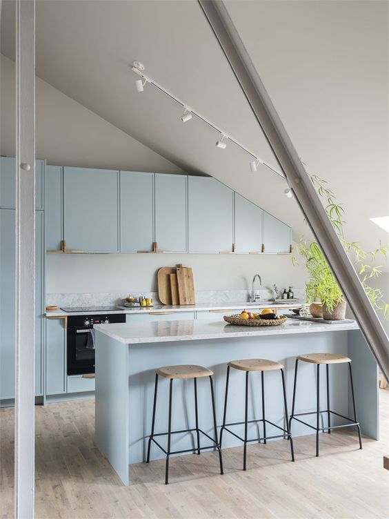 A light blue attic kitchen with elegant cabinets and a kitchen island, skylight, potted plant and stools is chic