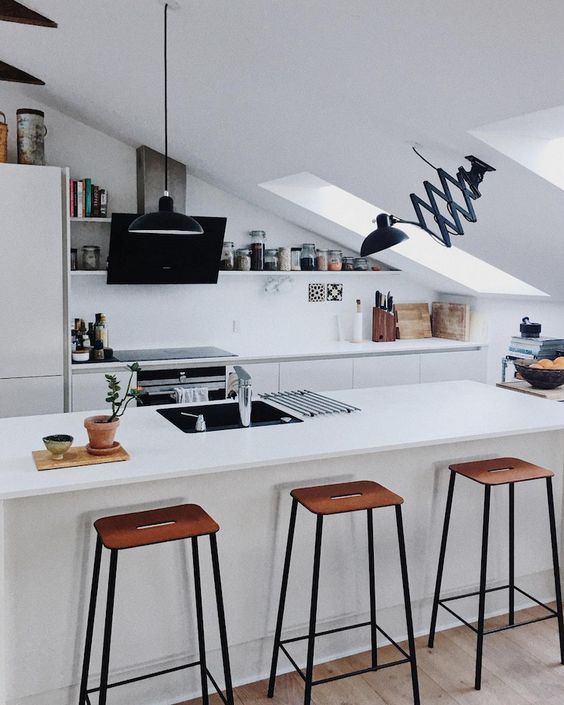 A minimalist attic kitchen with elegant cabinets, high stools, skylights and black fittings looks very stylish and bold